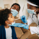 african-american-doctor-with-face-mask-examining-boy-s-throat-during-home-visit (1)